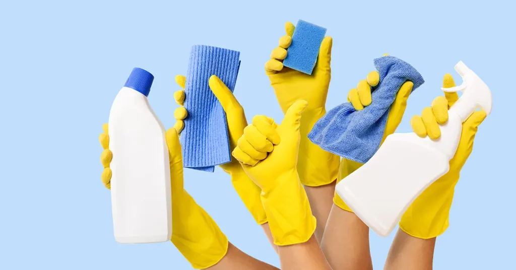 hand with yellow rubber glove holding cleaning supplies on blue background